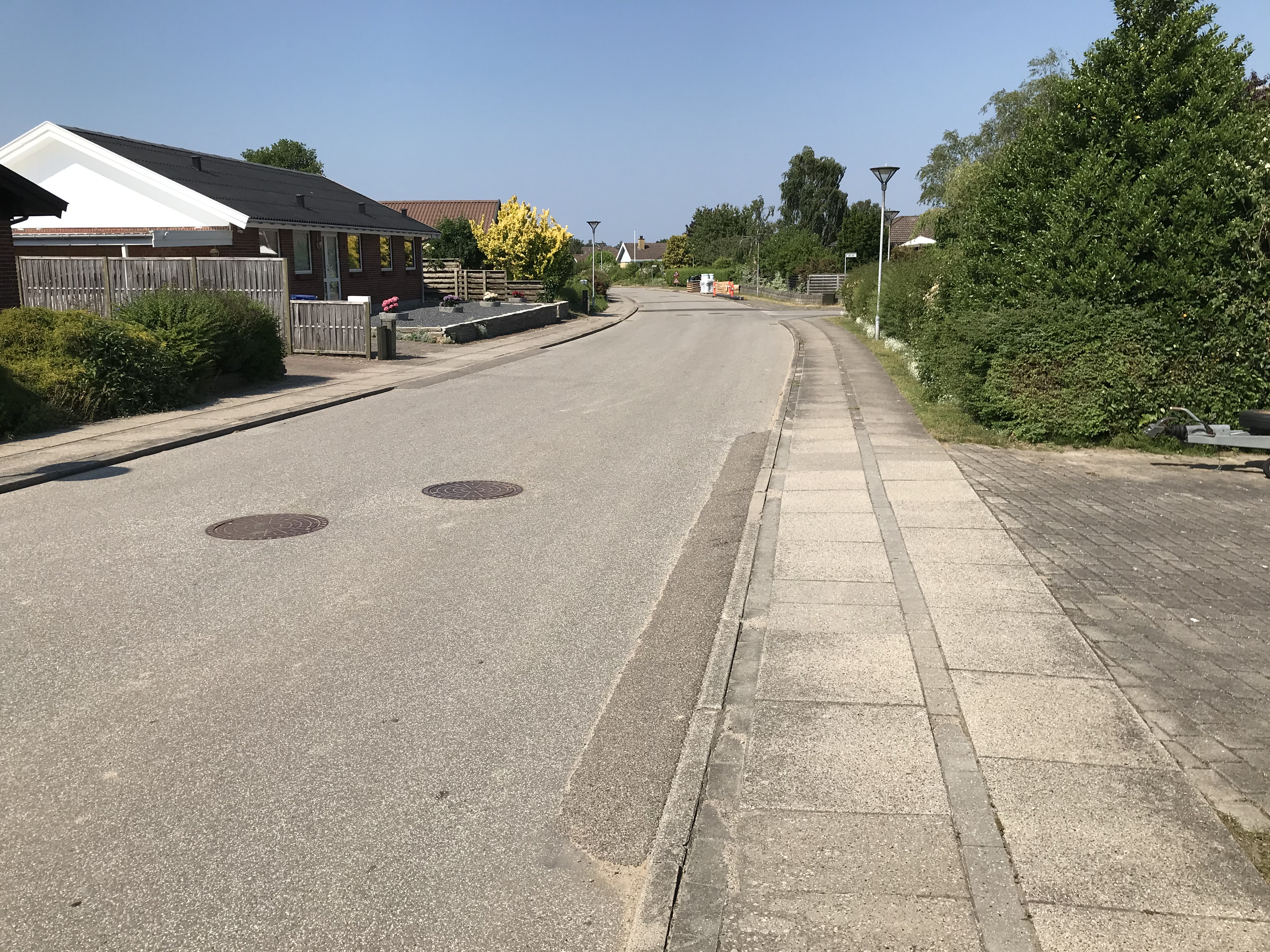 Villavej med kørebane og fortov med klassiske fortovsfliser - hækkene er grønne og himlen blå